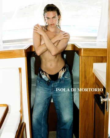 Adult woman posing semi-nude in a boat wearing jeans; soft window lighting