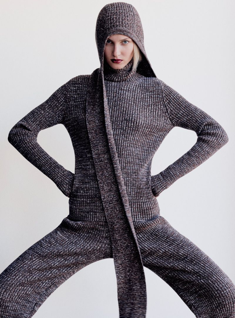 A fashion image shows a woman in a hooded ribbed knit sweater and pants, her hands on her hips, against a plain background.