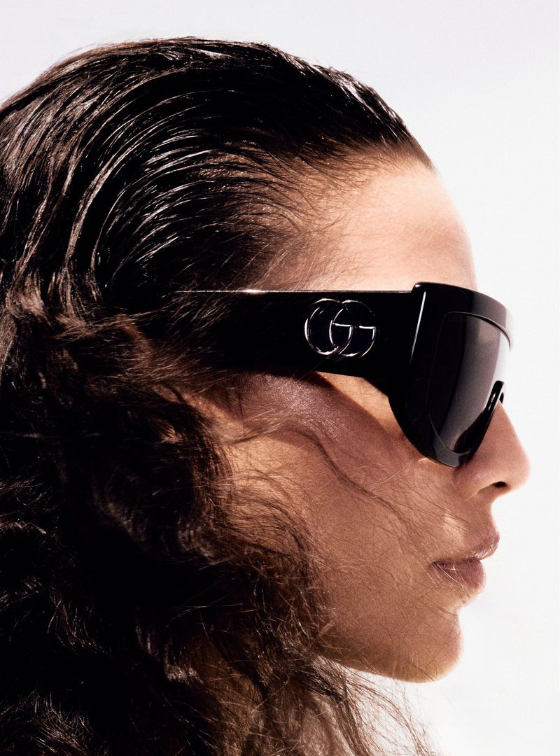 Side profile of a fashionable adult female with glossy black hair and large, modern black sunglasses with a silver 'GG' logo.