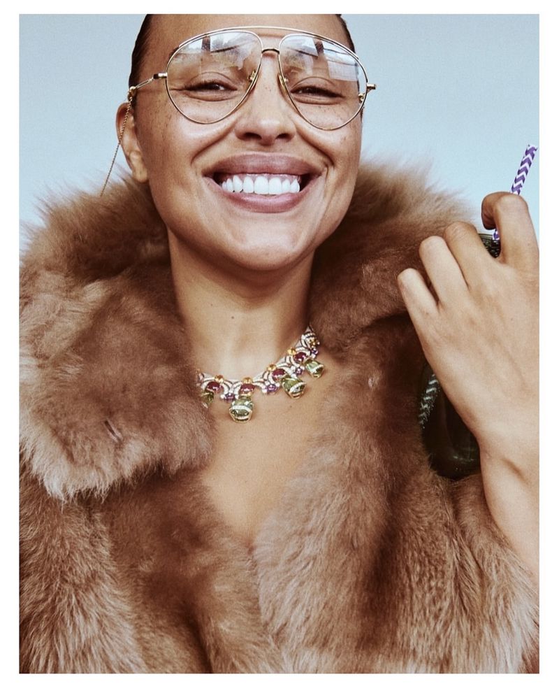 Smiling adult female wearing eyeglasses and a fur coat, holding a beverage with a straw. Close-up beauty shot with neutral background.