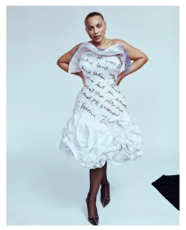 Model Paloma Elsesser in a white sculptural dress covered in handwritten text against a plain grey background