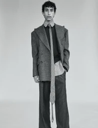 Model Rayan Mazuel posing in an oversized grey tailored jacket, wide trousers, and an extra-long necktie against a studio backdrop.