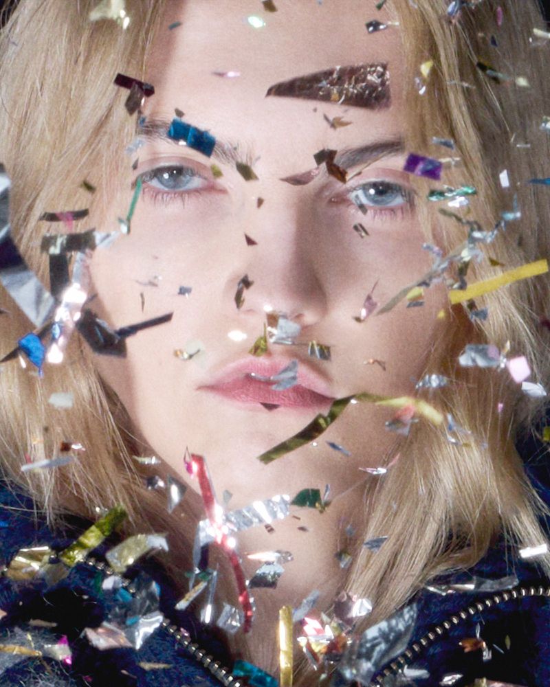 Close-up portrait of a blond woman with fair skin, surrounded by shiny confetti. Beauty shot with cool color grading and shallow depth of field.