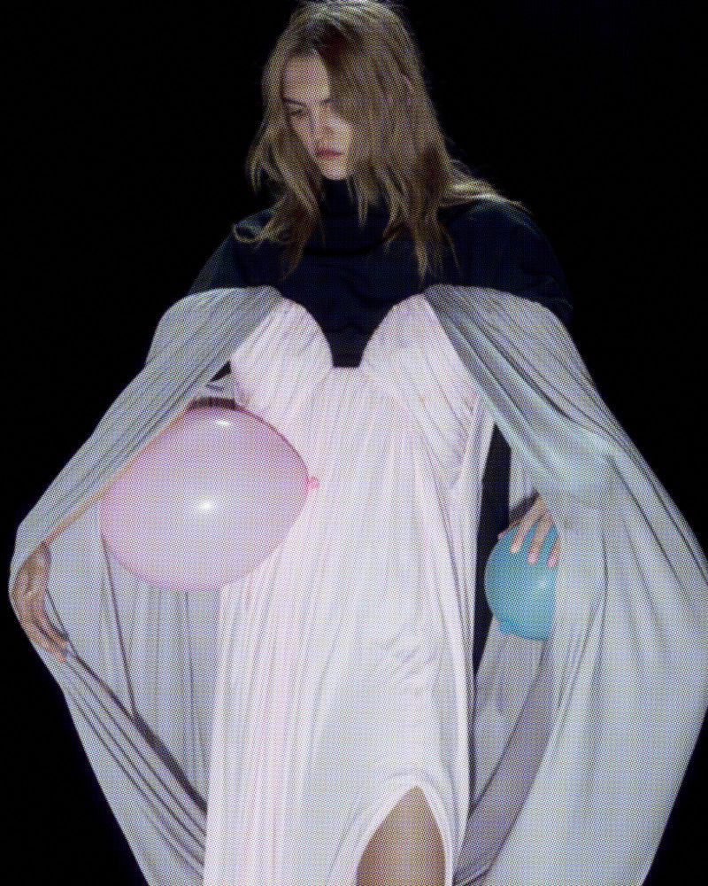 Fashion shot of a model in a dress, holding balloons in a studio against a black background, creating a dramatic visual.
