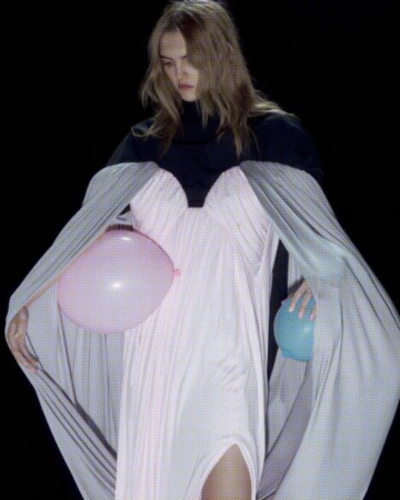 Fashion shot of a model in a dress, holding balloons in a studio against a black background, creating a dramatic visual.