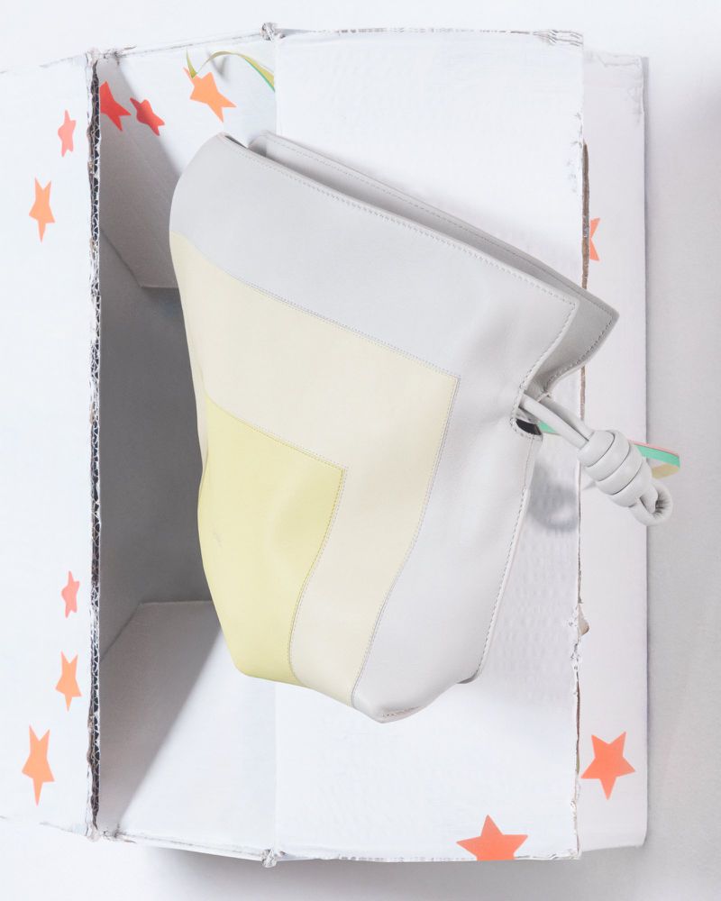 Stylish handbag with yellow, white, and grey color blocks, presented inside a decorative white cardboard box with orange stars.
