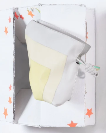 Stylish handbag with yellow, white, and grey color blocks, presented inside a decorative white cardboard box with orange stars.
