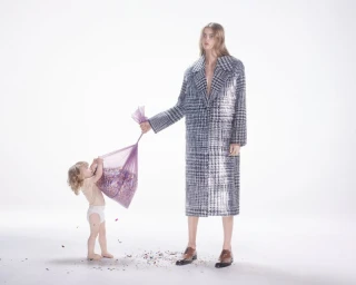 Woman in houndstooth coat and small child holding a purple bag of confetti against a plain white background