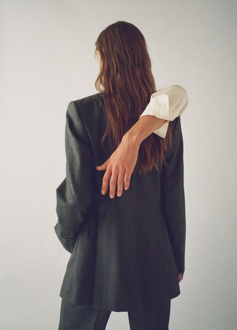 A woman in a suit poses with an arm around her, creating an intimate studio shot against a white backdrop, highlighting fashion and style.