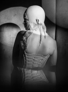 Model seen from behind wearing a lace-up corset and a bald cap headpiece with distressed lace trim in monochrome lighting.