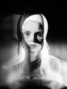 Portrait of a model with dramatic lighting, sculptural hair styling, and white textured face makeup in monochrome.