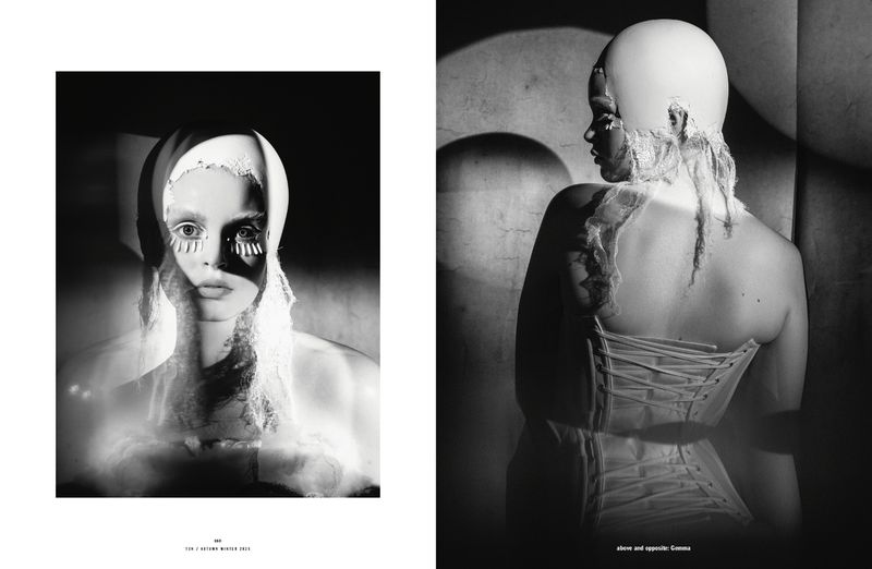 Monochrome studio shot features woman wearing white head covering and corset; bold eye makeup creates striking high fashion look.
