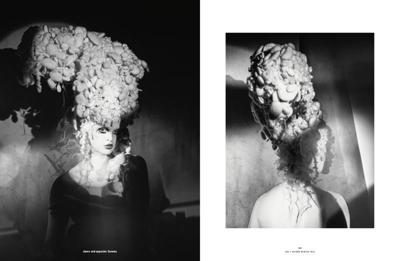 Dramatic black-and-white fashion editorial featuring a woman with elaborate headwear and makeup in a studio setting with moody lighting.