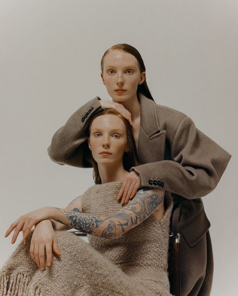 Fashionable studio portrait of two adult female models with red hair wearing wool and knit outfits against a neutral background.