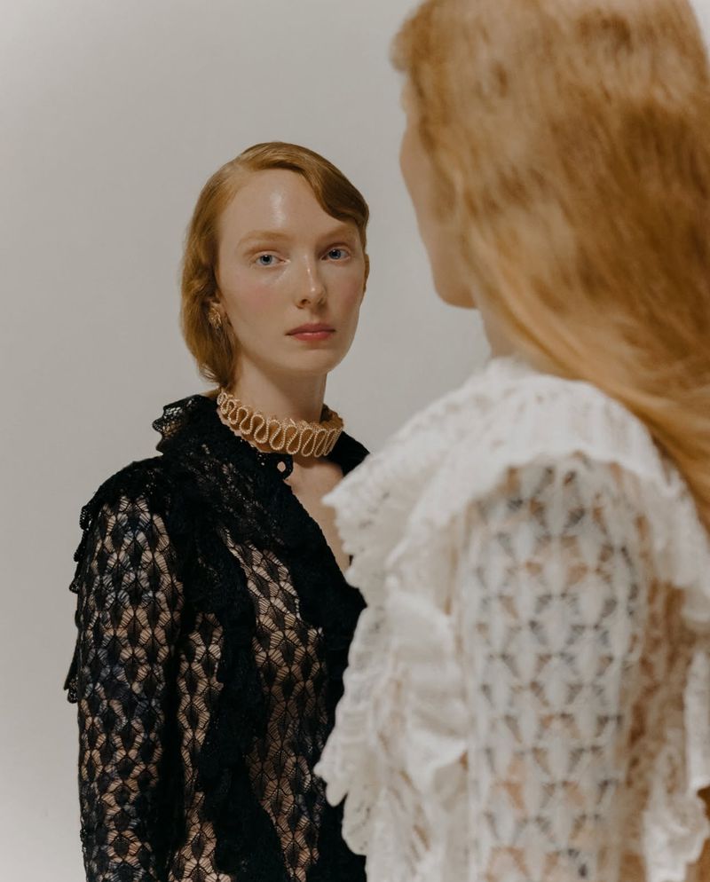 Two red-haired women in ruffled lace tops, one in black and one in white, pose in a minimalist photo studio. Beauty and fashion editorial.