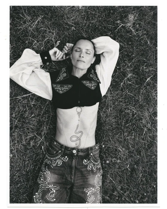 Model Tasha Tilberg lying in grass wearing embroidered vest and embellished denim jeans for Clin d'œil Magazine editorial
