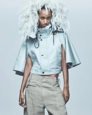 Fashion portrait of a Black woman with a feathered headpiece and blue jacket, posing in a photo studio with neutral background and lighting.