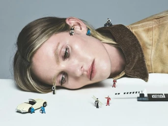 Close-up portrait of a woman reclining with miniature figures and tiny toy cars placed across her face and jacket.