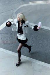 Model Tina Koveysha running across a city street wearing a white check tweed jacket and skirt set with black fur trim.
