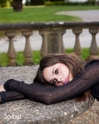 Model resting head on stone table outdoors wearing black long-sleeve top for Sorbet Magazine editorial