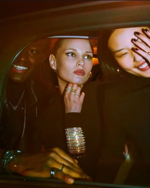 Three models wearing luxury diamond rings and bracelets posing together inside a dark car for an editorial shoot