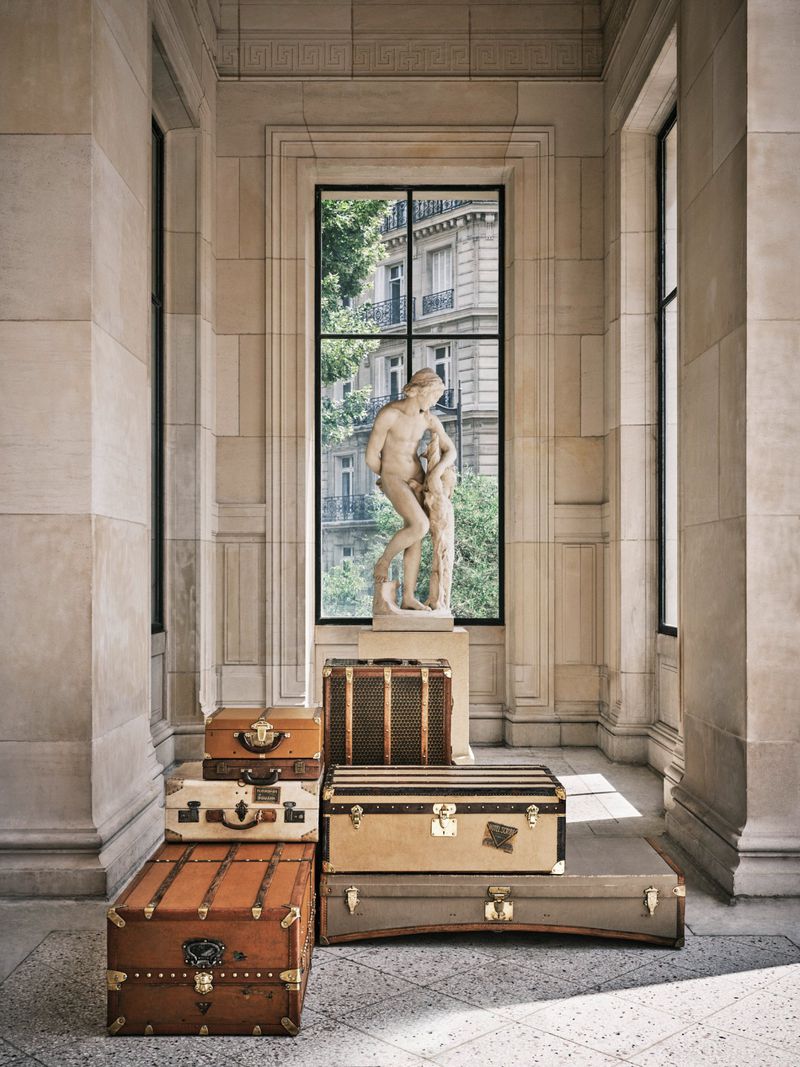 Vintage suitcases stacked in a beige stone hall with a classical statue in the background, showcasing luxury travel and artful composition.