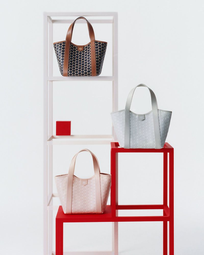 Three patterned tote bags in neutral colors are displayed on a modern red and white shelving unit against a bright white background.