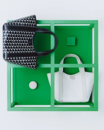 Two tote bags are displayed in a green and white cubical frame, one black patterned and one light grey, both facing the camera.