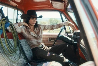 Kendall Jenner wearing a black cowboy hat and plaid shirt seated inside a vintage pickup truck for American Vogue.