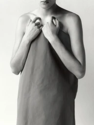 Monochrome portrait of model Noor Khan holding a draped strapless fabric garment against a neutral seamless backdrop.