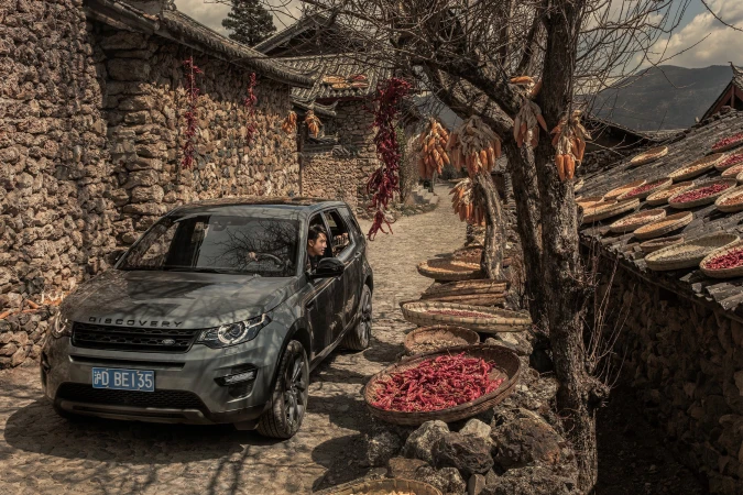 SUV parked on cobblestone street in rural village, China. Wicker baskets with red chilies and corn drying in the sun.