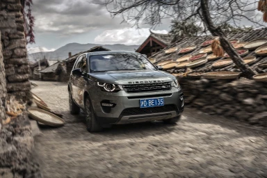Land Rover Discovery SUV driving along a narrow stone village street under an overcast sky, photographed by Jason Knott.