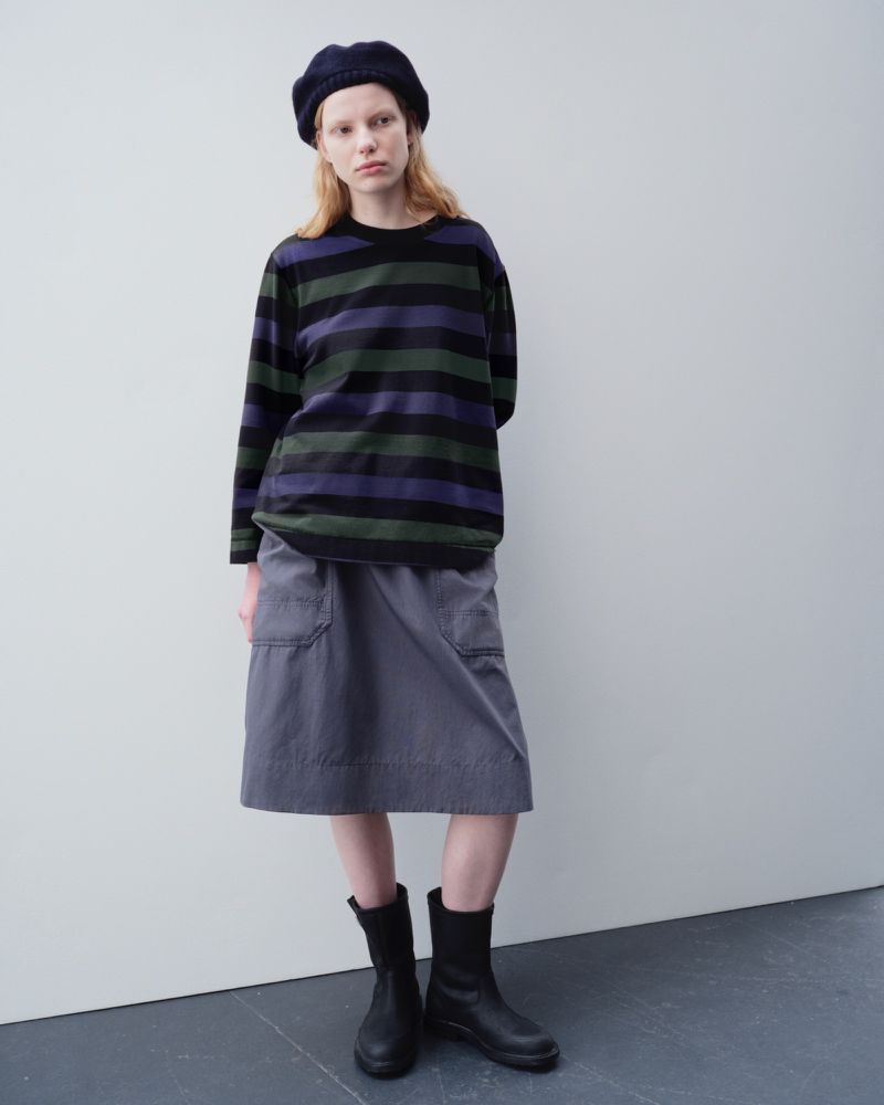 Full shot of a woman posing in a striped shirt, skirt, and boots against a simple studio backdrop. Fashion photography, soft lighting.