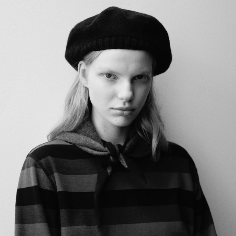 Monochrome portrait of a young adult woman wearing a beret and striped top, gazing directly at the camera in a studio setting.