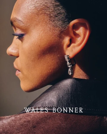 Close-up portrait of a woman in dark clothing, featuring diamond earrings, sleek hair, and makeup. Text overlay: WALES BONNER.