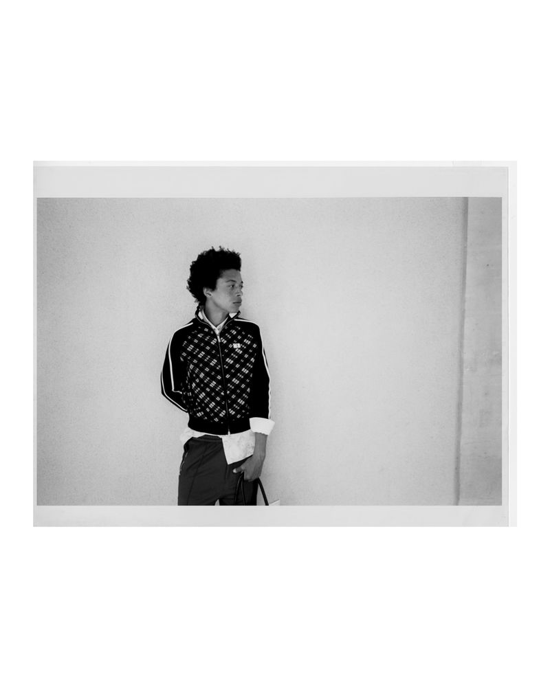 Black and white photo of a stylish adult wearing a patterned jacket and shirt, looking away from the camera indoors with soft lighting.
