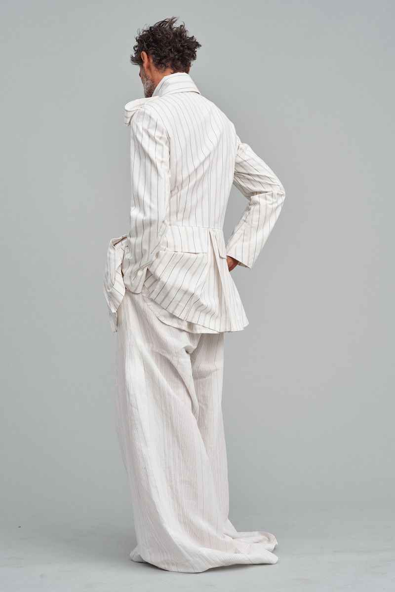 Back view of a stylish adult male in a striped suit, standing in a neutral studio setting, showcasing fashion and design.