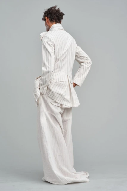 Back view of a stylish adult male in a striped suit, standing in a neutral studio setting, showcasing fashion and design.