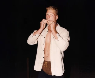 Blond man wearing an unbuttoned cream shirt against a dark background, photographed by Rob Tennent for Western Australia.