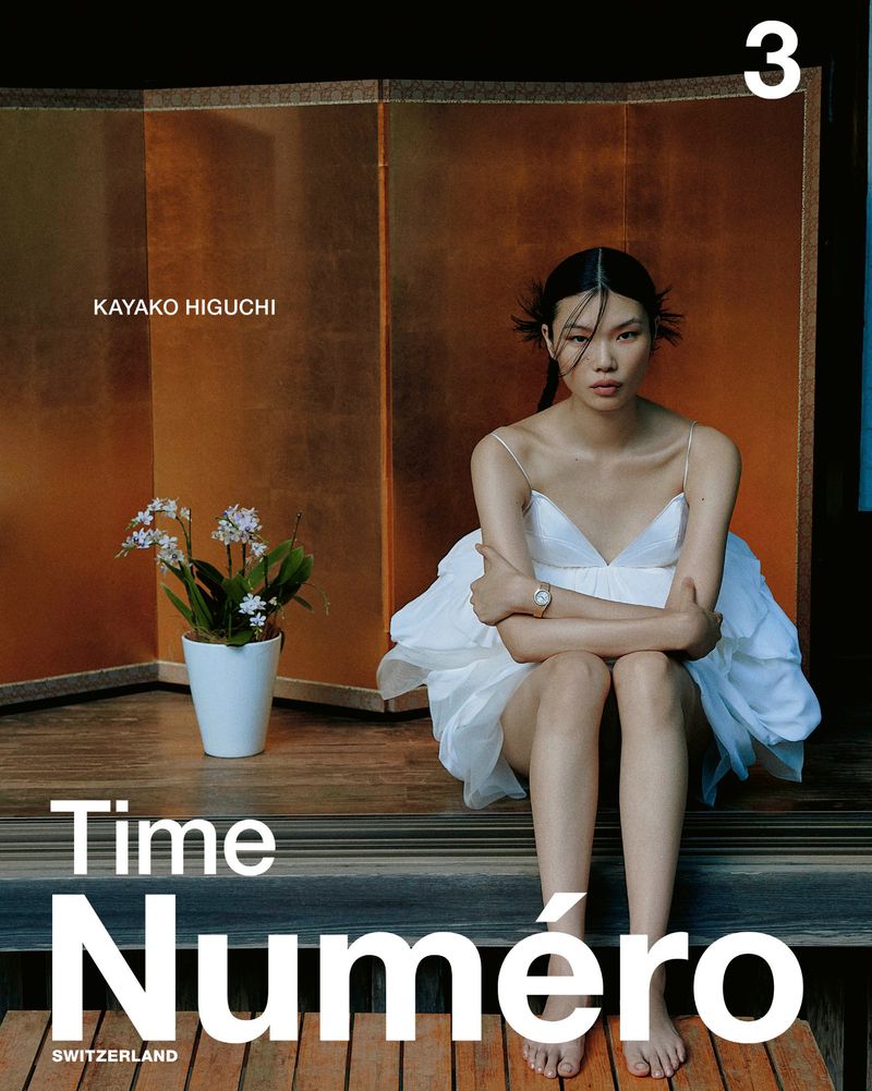 Asian woman in white dress poses near a houseplant and a gold screen for a Numero magazine cover, showcasing fashion and editorial style.