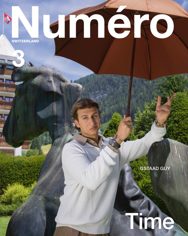 Magazine cover featuring a man holding an umbrella next to a sculpture of a cow, set in a Swiss landscape with mountains and buildings.