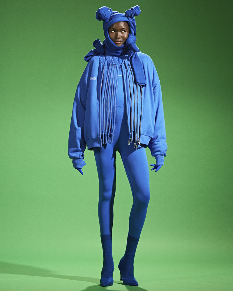 Woman in a bright blue monochrome outfit poses in front of a solid green backdrop in a studio shot for a fashion editorial.