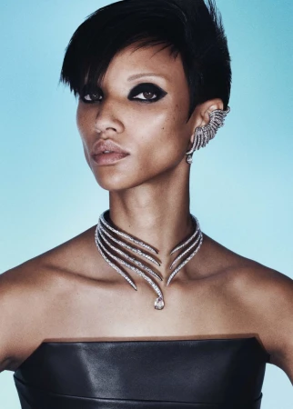 Close-up portrait of a woman with dark eye makeup wearing an ornate diamond necklace and matching ear cuff against a blue backdrop.