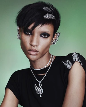 Model Georgia Palmer wearing crystal swan necklace, ear cuffs, and hair accessories in a black top against a green backdrop.
