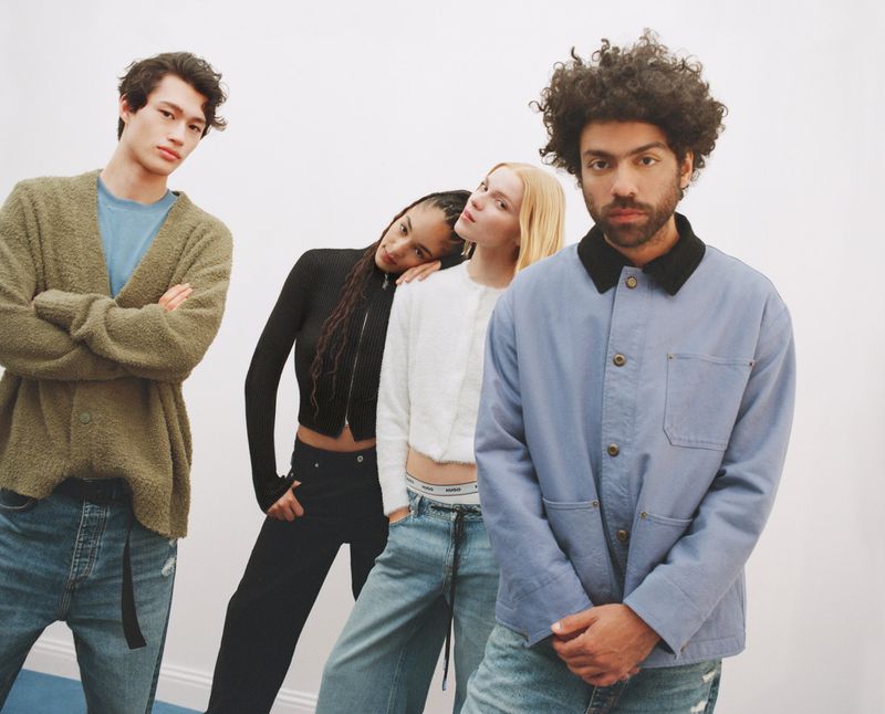 Four stylish young adults in casualwear pose in a neutral studio setting. Denim jeans, knit cardigans, and contemporary fashion.