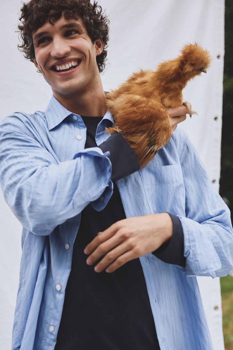 Smiling man in blue shirt holds fluffy brown chicken against white backdrop, creating a whimsical, eye-level close-up shot.