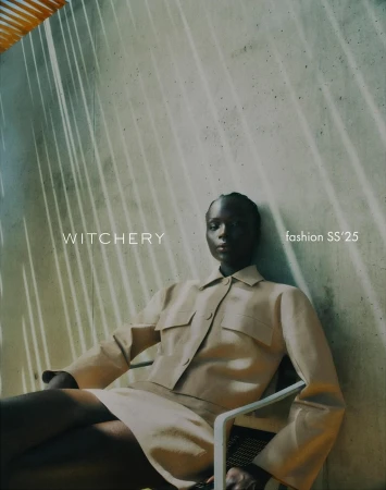 Fashion editorial shot of a Black woman in a matching tan skirt and shirt sitting in a chair in front of a concrete wall.