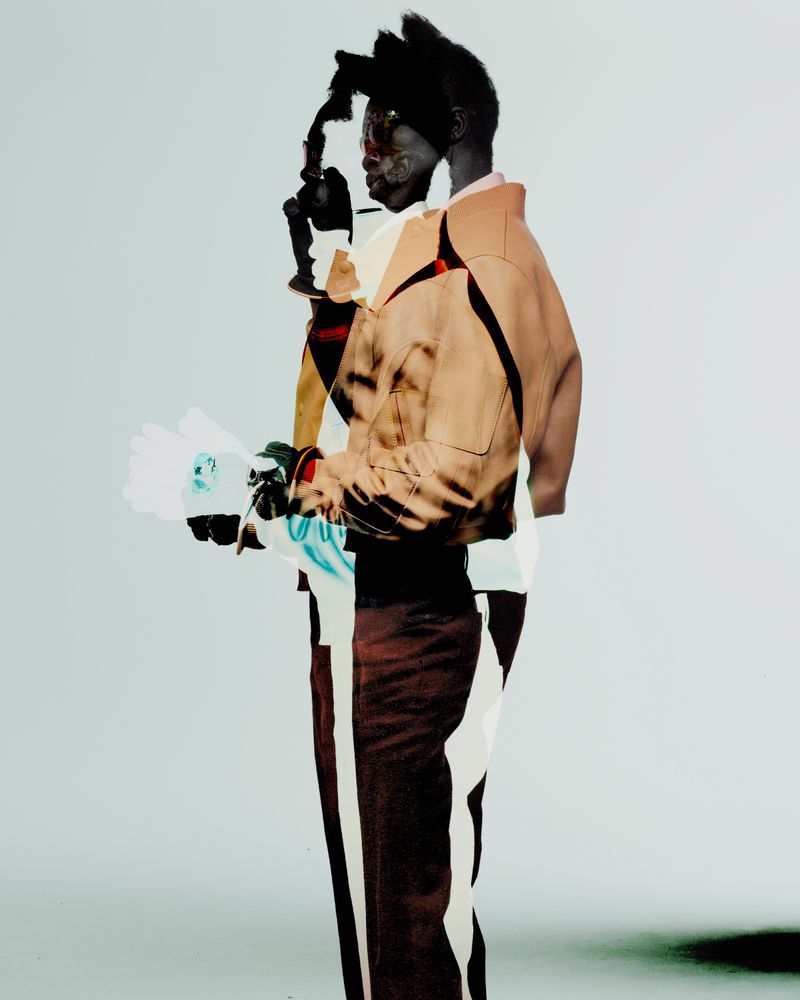 Double exposure portrait of an African American adult male model with modern tan coat and flowers set against a pale gradient background.