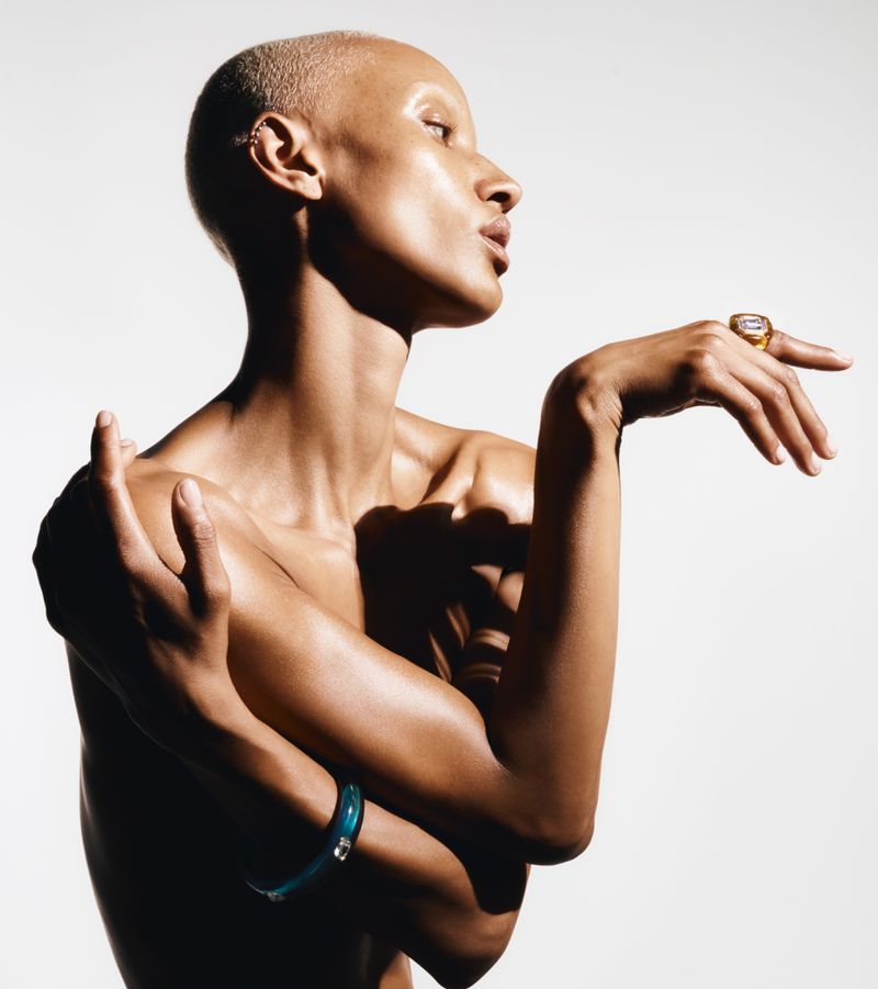 Portrait of a bald adult female model wearing jewelry, posing in a photo studio with even lighting and a white backdrop. Beauty shot.
