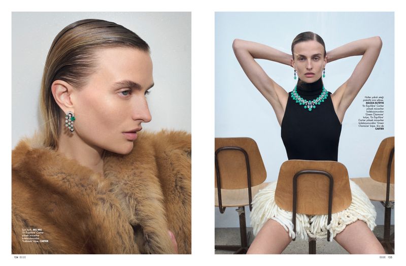 Editorial shot features a model wearing emerald jewelry and a fur coat; she poses between chairs in a studio with neutral lighting.